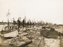 An old photograph depicting boats resting on a sandy beach, capturing a serene coastal scene from the past.