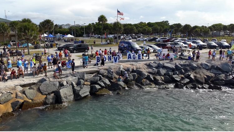 A crowd gathers by the water, with large letters spelling